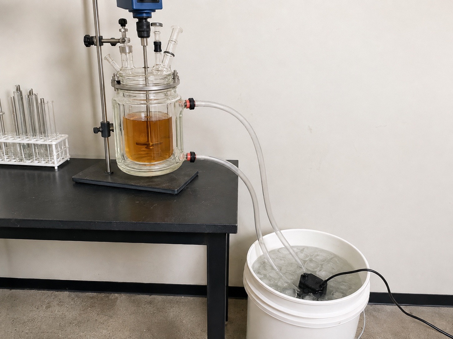 Budget cooling setup: a jacketed glass reactor holding amber CBD solution on a lab bench, connected by silicone tubing to a submersible pump sitting in a 5-gallon bucket of ice water on the floor
